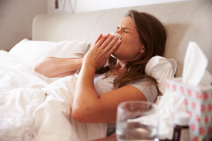 Bei Krankheit müssen Arbeitnehmer keinen betrieblichen Verpflichtungen nachgehen. Erkrankte junge Frau liegt im Bett und putzt sich die Nase.
